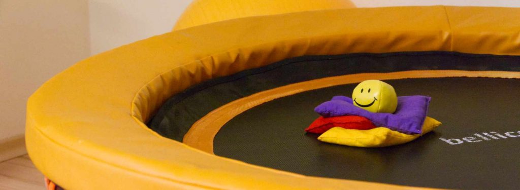 Motorik - Trampolin mit bunten Säckchen und lachendem Ball.
